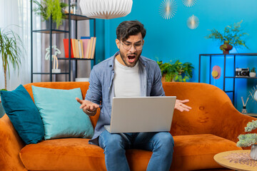 Angry sad Indian man use laptop notebook working, screaming shouting loses becoming surprised...