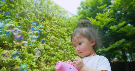 A young girl with an expression of wonder plays outdoors with a bubble blower, surrounded by...