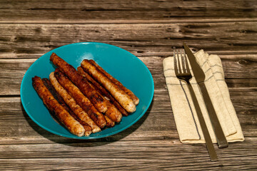 Plate sausages with a napkin, knife and fork on a wooden table