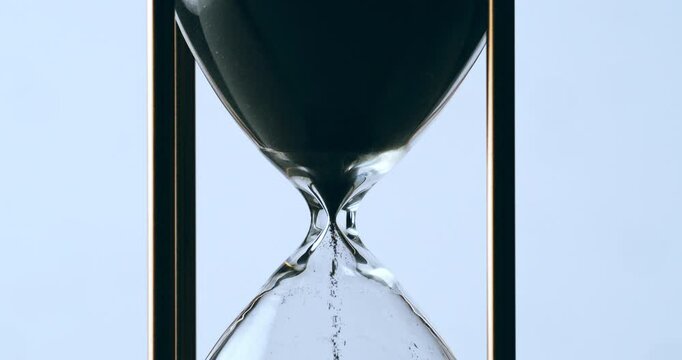 Super slow motion macro of fluid flow of black sand grains particles running inside hourglass sandglass clepsydra measuring passing time in countdown to deadline at 1000 fps.