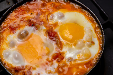 Shakshuka with tomatoes, peppers and onions is fried in a frying pan. Close-up