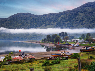 Sunrise at Puyuhuapi fjord in the Pacific Ocean, on rainy day, with nalcas flowers or pangue (Gunnera tinctoria) and fishing boats, Patagonia, Chile