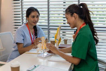 A woman is holding a model of a knee joint. She is talking to another woman who is looking at the model. Scene is educational and informative
