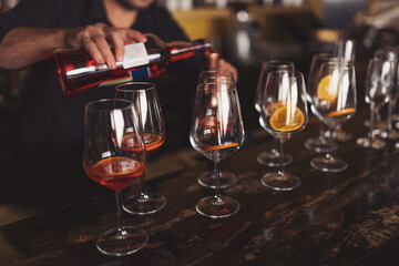 Making cocktail , process of preparation of a cocktail Aperol spritz. Glasses of alcoholic Aperol Spritz cocktail, aperol, prosecco, soda and slice of orange in large round glasses on party.