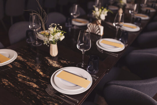 luxury tableware beautiful table setting in restaurant. banquette luxury arrangement plates and glasses. Glasses, forks, knives, napkins and decorative flower on a dark old brown wooden table. - Powered by Adobe