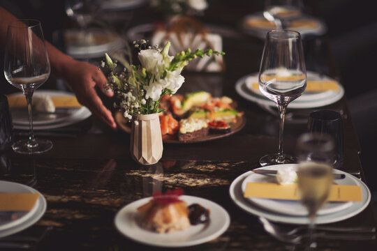 Crop waitperson serving table with wineglass in restaurant on blurred background.  woman setting up table for dinner party