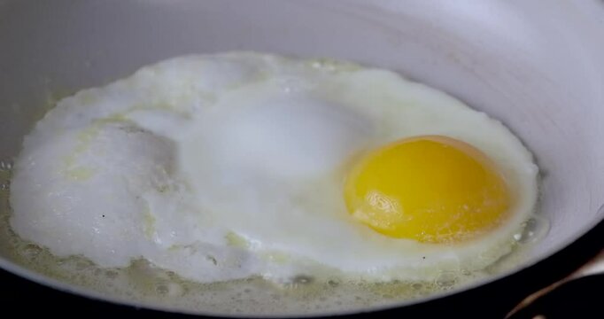 A fried egg with a yellow yolk sits in a pan. The egg is cooking and has a slightly runny yolk.