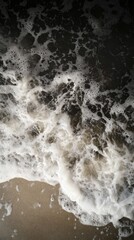 Close-up of ocean wave foam washing ashore on sandy beach.