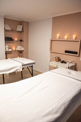 Massage therapy room featuring two massage tables covered with white linens, towels, calming candles, and hot stones for relaxing treatments. Wellness, tranquility, rejuvenation, spa and relax concept