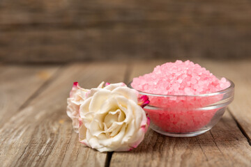 Sea salt for bath with aroma and rose flowers on textured wooden background. Pink sea salt. Spa treatments. Natural salt with herbs and essential oils. skincare concept. Meso for text. Copy space