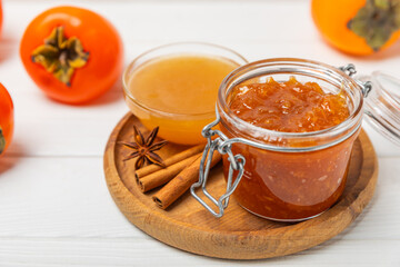 Persimmon jam with slices of ripe persimmon on wooden textured table. Delicious persimmon jam. Marmalade. Healthy sweets. Vegan. Close-up. Space for text. Copy space.