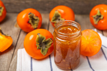 Persimmon jam with slices of ripe persimmon on wooden textured table. Delicious persimmon jam. Marmalade. Healthy sweets. Vegan. Close-up. Space for text. Copy space.