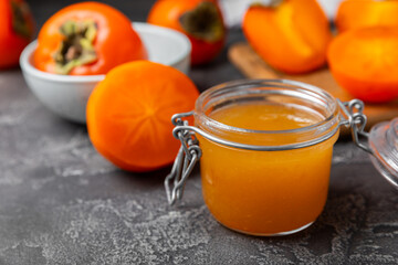 Persimmon jam with slices of ripe persimmon on wooden textured table. Delicious persimmon jam. Marmalade. Healthy sweets. Vegan. Close-up. Space for text. Copy space.