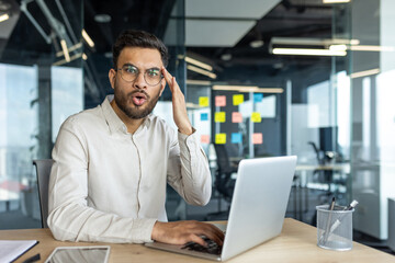 A Latin American businessman expresses surprise using a laptop in a modern office setting, conveying unexpected news or discovery. The environment reflects productivity and professional business