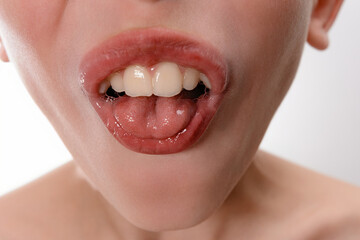 A detailed close-up shot focusing on a person's open mouth, showcasing healthy teeth and a slightly visible tongue. The image has soft lighting and a neutral background.