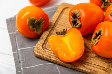 Persimmon on textured wooden background. Persimmon fruit. A piece of ripe, juicy, sweet persimmon fruit. Vegan. Orchard. Close-up. Space for text. Copy space.