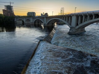 Sunrise over the city's river, with a dam and bridge. Water rushing over the dam. Urban landscape. Upper Dam, Minneapolis, Minnesota, United States