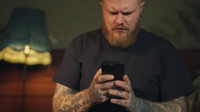 Handsome bearded man chatting online in mobile app, sitting alone in home room. Portrait of internet addicted male person with smartphone, user of mobile applications, play video games and commenting