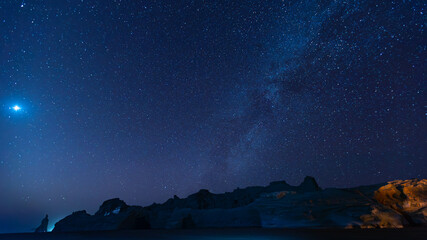 Starlit sky above rugged cliffs on a calm night by the coast