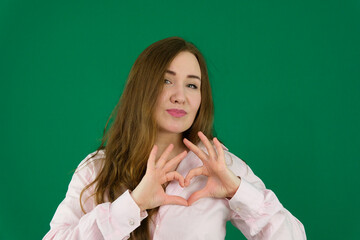 Attractive brunette young Asian woman feels happy and romantic shapes heart gesture expresses...