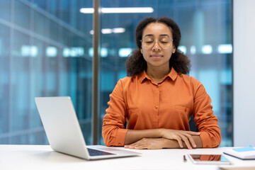 Young woman resting and relaxing inside office at workplace, businesswoman with closed eyes sitting and breathing with laptop, meditating.