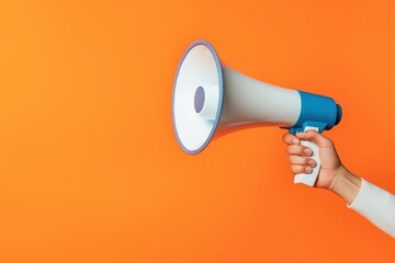 Hand holds megaphone against vibrant orange background. Public announcement concept. Communication tool. Possible scenarios include protest rally, news broadcast, social media promotion. Strategic