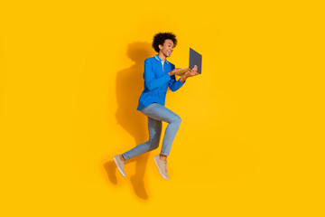 Full length photo of handsome young guy running hold netbook dressed stylish blue garment isolated on yellow color background