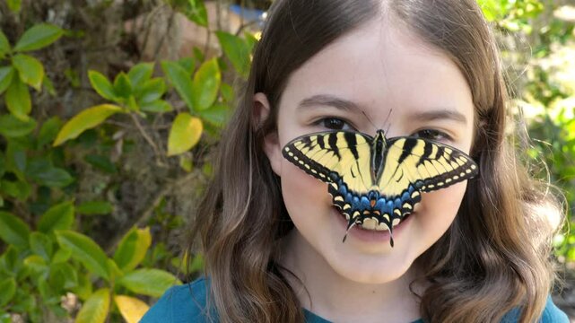 Little girl with large butterfly on her nose, smiling at camera.