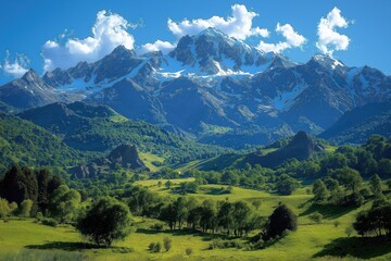 Fototapeta premium Majestic mountain range with snowy peaks dominates picturesque valley. Green meadows, forests scattered around valley. Plenty of trees, rocky outcrops visible in landscape. Clear sunny day creates