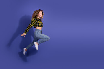 Young woman in a yellow plaid shirt jumping against a vibrant purple background