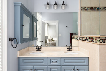 A bathroom with blue cabinet and medicine cabinet, a marble countertop, tiled shower, and view towards the primary bedroom.