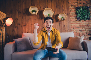 Excited young man enjoying leisure time in stylish living room with game controller