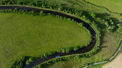 This image captures a stunning aerial view of a vibrant, green landscape where a winding river meanders through lush fields adorned with patches of trees and agricultural land.