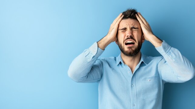 Frustrated man experiencing stress and anxiety with hands on head against a blue background expressing emotion