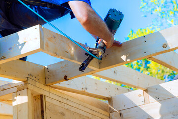 Carpenter works diligently, using air pneumatic nail gun to secure wooden beams during construction...