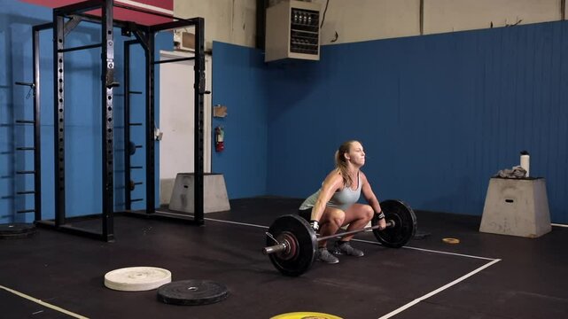 2/3 profile view of determined female power lifter lifting heavy weights over her head, then throwing them back down, slow motion shot.