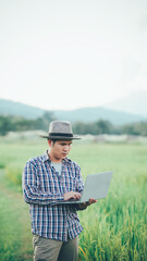 Happy Asian male farmer in the field Wear a hat and carry a smart tablet to track plant growth and disease. The concept of smart farmers using technology
