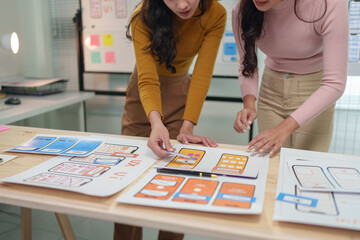 Fototapeta premium Two asian ux designers working together on a new project, pointing at wireframes and discussing user interface improvements for a mobile application
