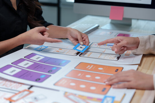 Web designers are discussing user experience and user interface details for a new mobile application by analyzing wireframes and prototypes printed on paper