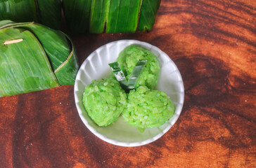 Green sticky rice tape shaped into a ball served on a plate. Indonesian sticky rice tape wrapped in banana leaves on a wooden table