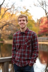 Young Man Smiling in a Plaid Shirt by a Scenic Lake in Autumn