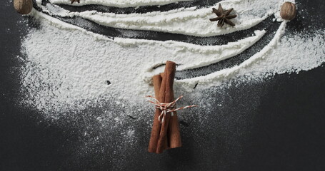 Cinnamon sticks tied with string lie amidst flour on a dark surface © vectorfusionart
