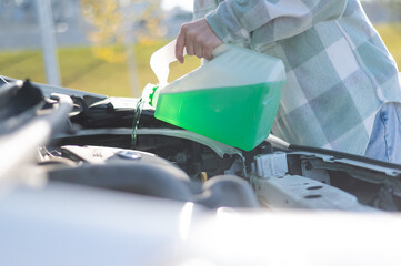 Close up of female hands filling car reservoir with windshield washer fluid from bottle. 