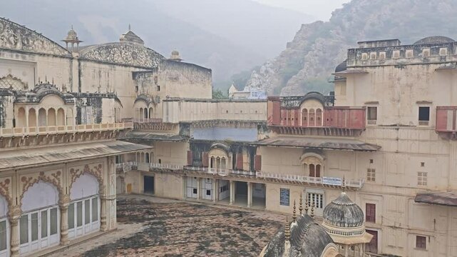 Expansive Alwar Fort courtyard surrounded by greenery, overlooking misty mountains on a cloudy day.