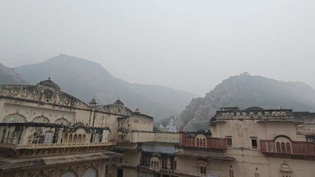 Expansive Alwar Fort courtyard surrounded by greenery, overlooking misty mountains on a cloudy day.