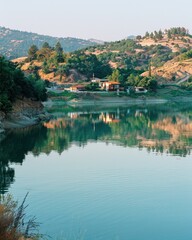 Serene lake reflecting hillside village and lush greenery under a clear sky.