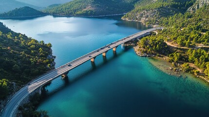 Serene Bridge Over Turquoise Waters: An aerial view captures a long bridge gracefully spanning a stunning turquoise lake nestled amidst lush green mountains.