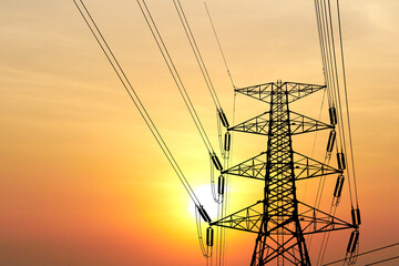 High Voltage Power Line Tower Silhouetted Against a Vibrant Sunset Sky with Orange and Yellow Hues