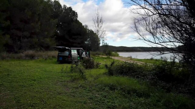 4K Drone footage of woman having breakfast at a Camper van in nature with stunning lake and forest view somewhere in Valencia, Spain. High quality 4k footage
