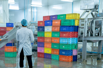 A factory worker wearing protective gear, organizing colorful storage crates in a clean and modern industrial facility, showcasing efficiency, cleanliness, and organization in industrial operations.